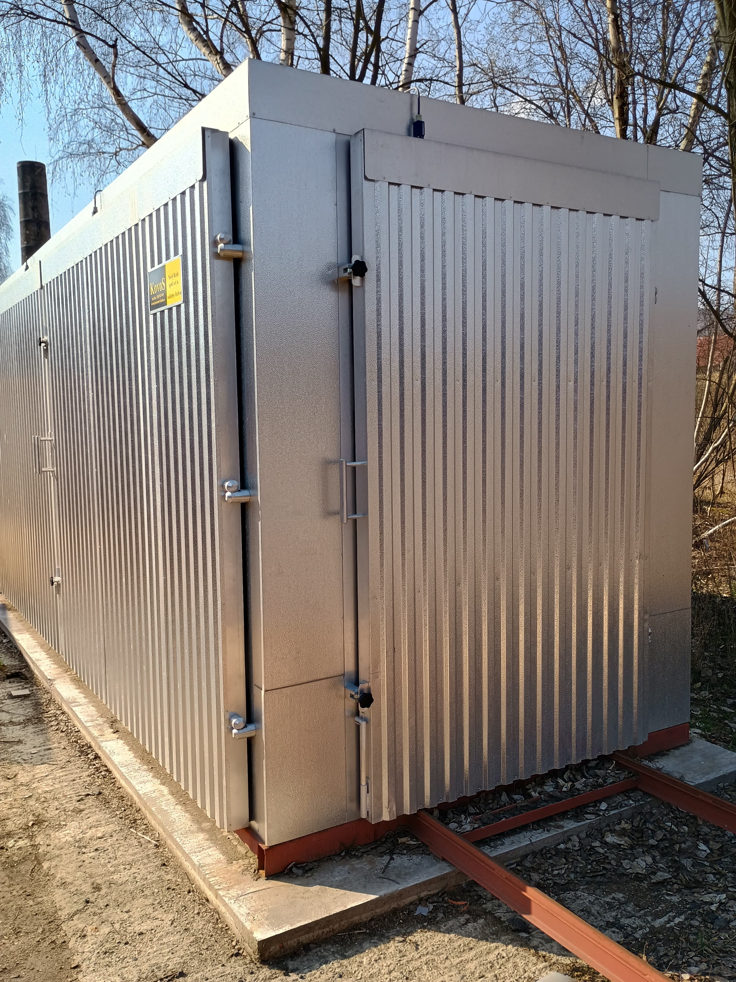 Silver corrugated metal industrial enclosure with access doors on a concrete base outdoors.